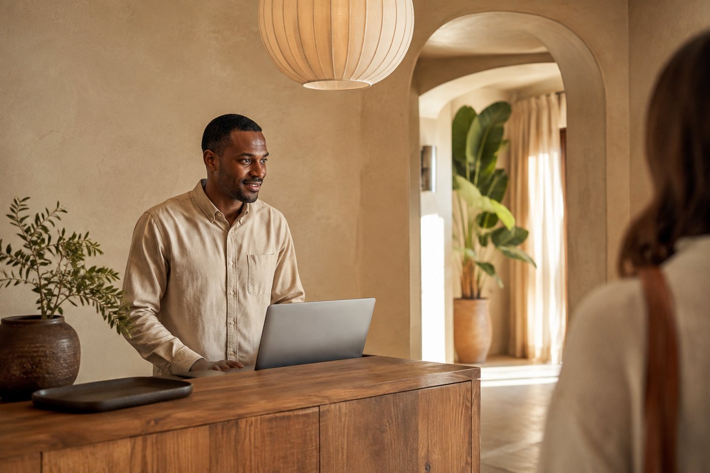 A receptionist welcoming a guest at a warm, sunlit hotel reception.